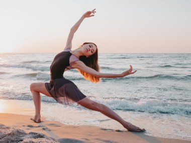 Gün doğumu veya gün batımında okyanus veya deniz yakınında set üzerinde siyah ipek elbise dancing balerin. Uzun saçlı genç kadının silueti duyguları ile klasik egzersizler pratik