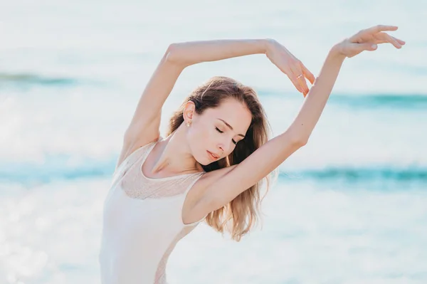 Retrato de mujer joven con pelo largo practicando ejercicios clásicos con emociones.Bailarina bailando en vestido de seda blanca en terraplén cerca del océano o el mar al amanecer o al atardecer . — Foto de Stock