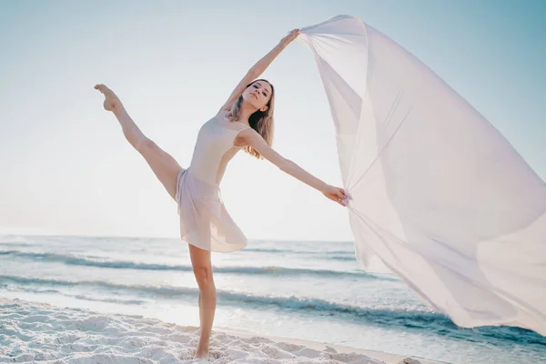 Joven hermosa bailarina bailando ballet en la orilla del mar con gran tela de seda revoloteando en el viento.Concepto de ternura, ligereza, arte y talento en la naturaleza — Foto de Stock