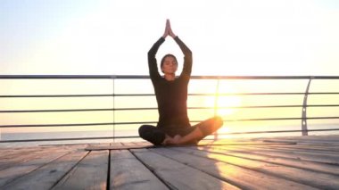 Siyahlar içindeki kız yoga meditasyonunda pratik yapıyor, nefes egzersizleri yapıyor, ahşap deniz kenarında pranayama yapıyor. Lotus pozu veren kadın. Sağlıklı yaşam tarzı kavramı