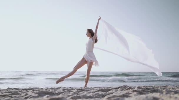 Flexible Turnerin tanzt auf dem Meer, riesige Seidenstoffe flattern im Wind — Stockvideo