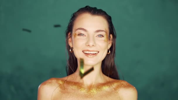 Portrét krásné ženy se zlatým make-upem, usmívající se jiskry a konfety na tyrkysovém pozadí. Štěstí, radost, párty, oslava konceptu. — Stock video