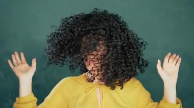 Kıvırcık saçlı güzel bir kadın. Stüdyoda turkuaz arka planda gülümseyip dans ediyor. Müzik, dans konsepti, ağır çekim