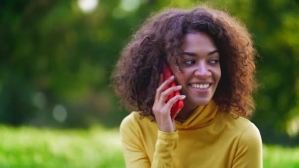 Sonriendo hablando por teléfono móvil sobre verde. De cerca hermosa mujer de raza mixta — Vídeos de Stock