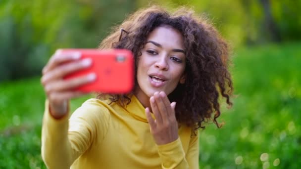 Όμορφη γυναίκα χρησιμοποιεί κόκκινο κινητό τηλέφωνο στο πάρκο. Κορίτσι με κίτρινα που βγάζει σέλφι — Αρχείο Βίντεο