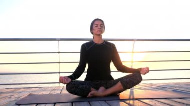 Yoga meditasyonunda siyahlar içindeki konsantre kız ahşap deniz kenarında meditasyon yapıyor. Lotus pozu veren kadın. Esneme, pratik, sağlıklı yaşam tarzı konsepti