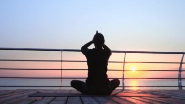Siyahlar içindeki kız yoga meditasyonunda pratik yapıyor, nefes egzersizleri yapıyor, ahşap deniz kenarında pranayama yapıyor. Lotus pozu veren kadın. Sağlıklı yaşam tarzı kavramı