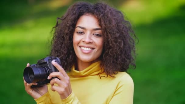 Молода африканка в жовтому робить фотографії з камерою DSLR зеленого фону — стокове відео