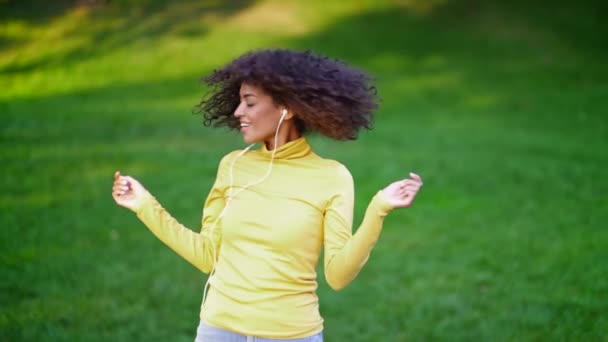 Menina adolescente Africano ouve música com fones de ouvido park.Cute mulher em amarelo — Vídeo de Stock