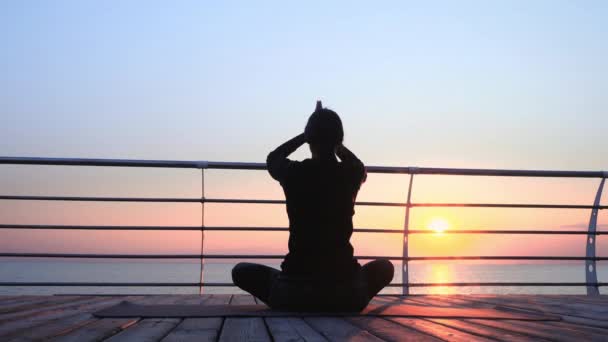 Fille en noir pratiquant la méditation de yoga, faire des exercices de respiration pranayama sur le front de mer en bois. Femme en pose de lotus. Concept de mode de vie sain — Video