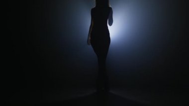 Karanlık duman odasında dans eden ve spot ışıklarının önünden geçen seksi bayan dansçı. Yavaş çekim