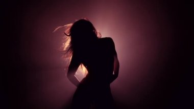 Dumanlı, karanlık arka planda güzel dansçı silueti. Spot ışığı seksi kıza geri yansıyor. Baştan çıkarıcı hareket ediyor..