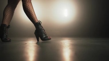Yüksek topuklu bir kız dumanlı sahnede kameranın önünden geçiyor. Seksi elbiseli kadın. Gece kulübü dansçısı konsepti.