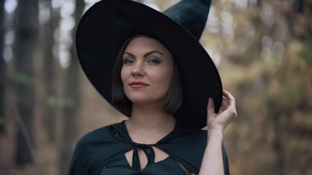Portrait of young pretty witch in cap on autumn forest background. Halloween concept, cosplay dressing up. Slow motion — Stock Video