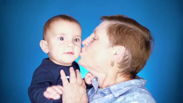 Grootmoeder met baby boy ion blauwe muur achtergrond hebben plezier, glimlachen, spelen. Kleinzoon communiceert graag met oudere overgrootmoeder. — Stockvideo