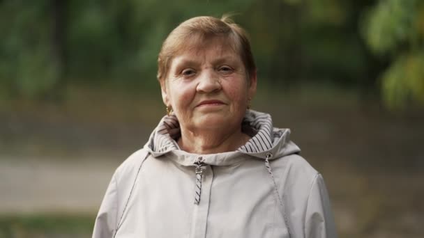 Piękny portret uśmiechniętej starszej kobiety w jesiennym parku. Biała babcia patrząca w kamerę. — Wideo stockowe
