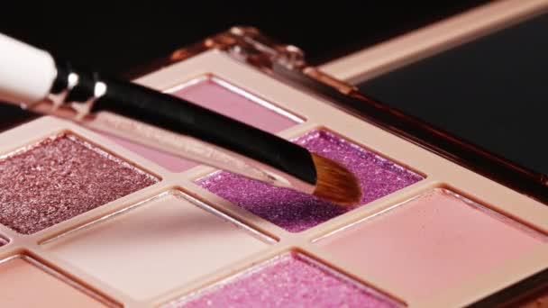 Penseel krijgt roze pigment op stapel te gebruiken in make-up. Kunstenaar werkt met oogschaduwen palet, verschillende poeder kleuren. Details van het werkproces, gereedschappen in de schoonheidsindustrie. Decoratieve cosmetica. — Stockvideo
