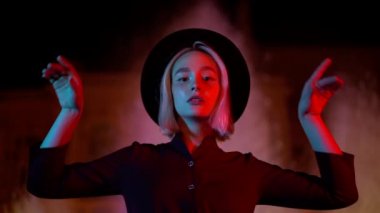 Yeni nesil hippi kadın portresi. Sarı saçlı, neon fıskiyeli arka planda duruyor. Geceleri şehir. Şapka, burun piercing 'i. Güzel, çekici bir kız. Yavaş çekim.