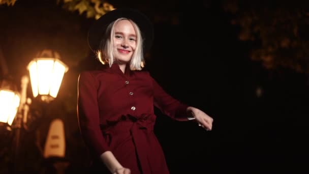 Millennial hipster vrouw met blond haar dansen onder de lantaarn van de stad straat 's nachts. Hoed, neuspiercing. Grappig meisje. Langzame beweging. — Stockvideo