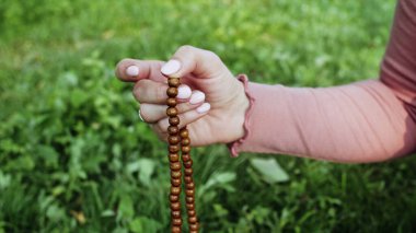 Elini yakan kadın tespihi de sayıyor. Mantra meditasyonları sırasında saymak için kullanılan değerli boncuk iplikleri. Kız yaz doğasında oturuyor..