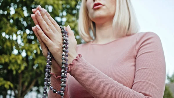 Womans hands with mala beads or rosary together symbolizing prayer and gratitude. Mudra. Yoga concept. Concentrated girl standing with hands in namaste and meditating or praying.