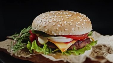 Biberiyeli büyük iştah açıcı burger, et pirzolası, soğan, sebze, erimiş peynir, marul ve parşömen üzerine mayonez sosu. İzole edilmiş hamburger koyu duman arka planında döner, yakın plan görüntüsü