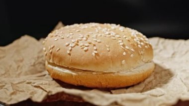Hamburger veya hamburger yapmak için ev yapımı susamlı çörekler parşömen üzerinde döner. Yakın çekim görüntüsü. Sağlıksız bir yaşam tarzı. Yemek, siyah arka plan. 4k