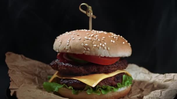 Grote smakelijke hamburger met vleessnijder, ui, groenten, gesmolten kaas, sla en mayonaise saus. Geïsoleerde hamburger draait op donkere rookachtergrond, close-up zicht — Stockvideo