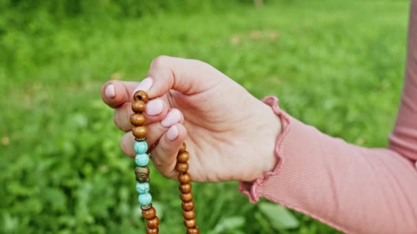 Mujer iluminada mano cerca cuenta rosario - malas hebras de piedras preciosas perlas utilizadas para mantener el recuento durante las meditaciones del mantra. Chica se sienta en la naturaleza de verano. Movimiento lento . — Vídeo de stock