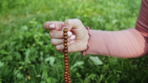 Рука молодой верующей женщины молится в природе и использует ремесленные четки для подсчета молитвы и сосредоточиться на медитации. Религия, надежда, концепция любви. Медленное движение . — стоковое видео
