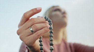 Elini yakan kadın tespihi de sayıyor. Mantra meditasyonları sırasında saymak için kullanılan değerli boncuk iplikleri. Kız yaz doğasında oturuyor. Yavaş çekim.
