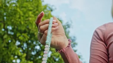 Elini yakan kadın tespihi de sayıyor. Mantra meditasyonları sırasında saymak için kullanılan değerli boncuk iplikleri. Kız yaz doğasında oturuyor. Yavaş çekim.