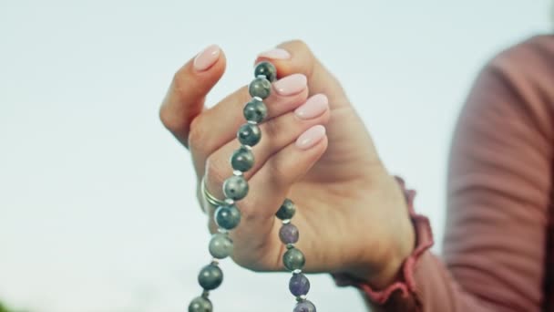 Mujer iluminada mano cerca cuenta rosario - malas hebras de piedras preciosas perlas utilizadas para mantener el recuento durante las meditaciones del mantra. Chica se sienta en la naturaleza de verano. Movimiento lento . — Vídeo de stock