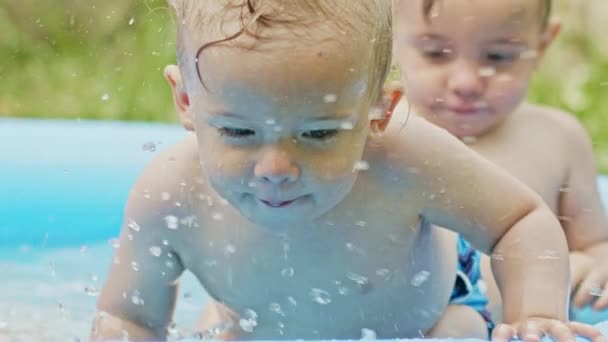 Småpojkar tvillingar simmar tillsammans i blå utomhuspool. Bröder ler, har roligt, njuta av stänk vatten. Begreppet hälsosam livsstil, familj, fritid på sommaren. Långsamma rörelser. — Stockvideo