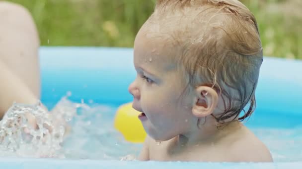 Bahçede mavi sokak havuzunda banyo yapan şirin küçük çocuk. Neşeli bir bebeğin portresi, bebeğim. Çocuk güler, su sıçratır, gülümser. Sağlıklı yaşam tarzı, aile, yazın boş zaman kavramı. Yavaş çekim. — Stok video