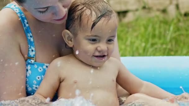 Мама плавает с маленьким мальчиком в голубом открытом бассейне. Мама и сын улыбаются, веселятся. Концепция здорового образа жизни, семьи, досуга летом. Медленное движение . — стоковое видео