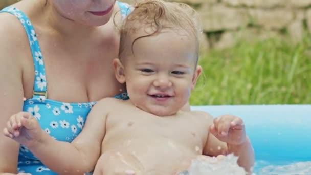 青い屋外プールで小さな男の子と母親の水泳。ママと息子は笑って、楽しんでいます。健康的なライフスタイル、家族、夏のレジャーの概念。スローモーション. — ストック動画