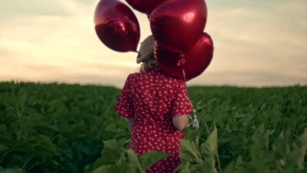 Hübsche Frau in rotem Retro-Kleid posiert mit herzförmigen Luftballons im grünen Feld. Mädchen mit Strohhut oder Baskenmütze. Geburtstag, Feiertag, Freiheitsbegriff. — Stockvideo