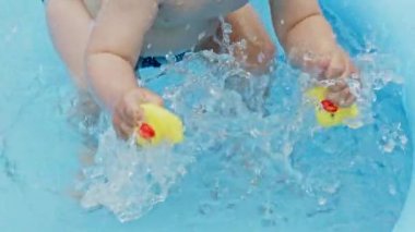 Childs 'ın sarı lastik ördekli elleri yazın açık havuzda yüzerken su sıçratır. Küçük oğlan eğleniyor. Sağlıklı yaşam tarzı, aile, yazın boş zaman kavramı. Yavaş çekim.