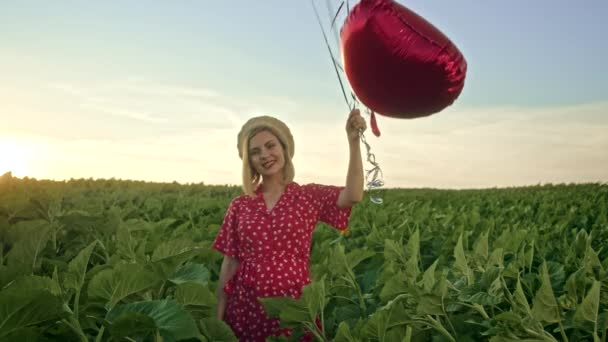 Mujer bonita en vestido rojo retro posando con globos en forma de corazón en el campo verde. Chica en sombrero de paja vintage o boina. Cumpleaños, vacaciones, celebrar el concepto de libertad . — Vídeos de Stock