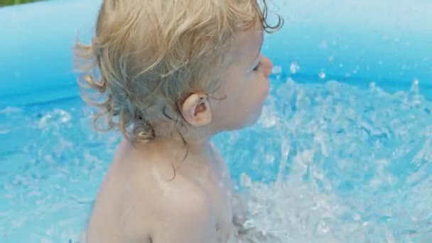 中庭の青い通りのプールで快適な小さな赤ちゃんの水泳。楽しい幼児の肖像画。子供は笑う、水をこぼす、笑顔。健康的なライフスタイル、家族、夏のレジャーの概念。スローモーション. — ストック動画