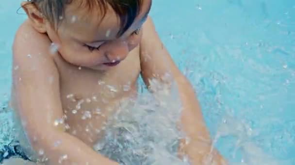 Leuk klein kind badend in een blauw straatzwembad op de binnenplaats. Portret van een vrolijke peuter, baby. Hij lacht, spat water, glimlacht. Concept van gezonde levensstijl, familie, vrije tijd in de zomer. Langzame beweging. — Stockvideo