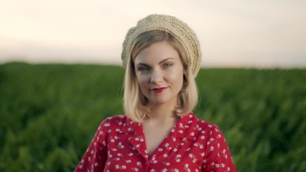 Prachtig portret van aantrekkelijke blonde vrouw met strobaret hoed op groene natuur achtergrond. Retro bloemenjurk, rode lippen. Aangenaam vrouwelijk uiterlijk, vriendelijke glimlach. 4k slow motion — Stockvideo