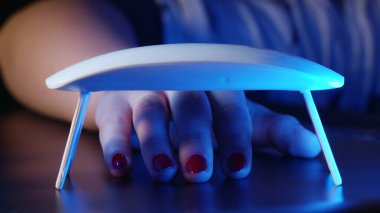 Kadın evde tek başına kırmızı jel cilasıyla oje sürüyor. Manikür için ultraviyole lamba. Ellerle çalışmanın modern metodu. Ultraviyole alet, ana ekipman