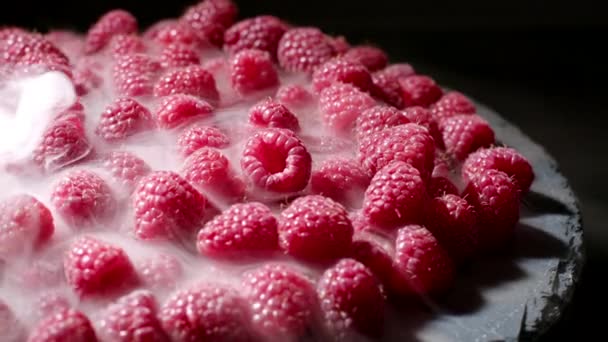 Reife gekühlte rote Himbeeren mit Trockeneisdampf isoliert auf dunklem Hintergrund. Ernährung, Vitamine, Antioxidantien. Blick auf köstliches Dessert. — Stockvideo