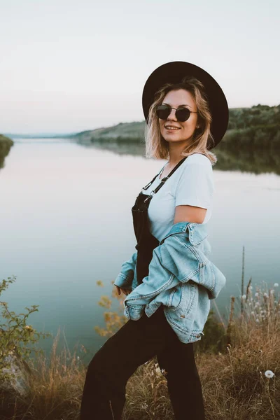 Giovane donna alla moda hipster in cappello nero e dungaree. — Foto Stock