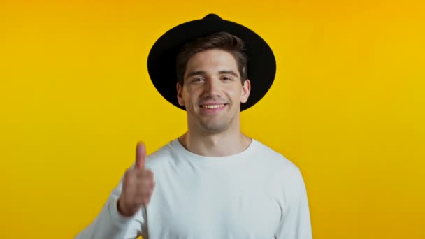希斯特的家伙在黄色背景上露出大拇指的痕迹.一个积极向上的年轻人对着摄像机笑.赢了成功。身体语言. — 图库视频影像