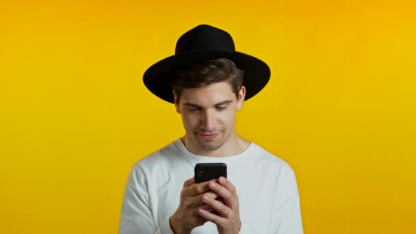 Handsome hipster man texting in messenger and receiving frustrating sms. Guy sighs. Yellow studio background. Technology, smartphone, modern technical capabilities concept — Stock Video