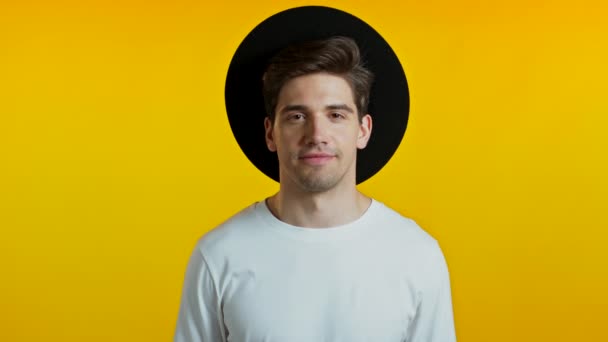 黄色のスタジオの背景に帽子で流行のヘアドアを持つハンサムなヨーロッパの男。陽気な男笑顔とカメラを見て. — ストック動画