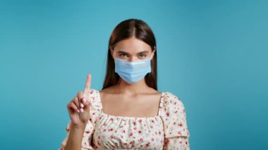 Tıbbi maskeli bir kadın hiçbir işaret olmadan bunu onaylamıyor. Reddetmek, reddetmek, anlaşmazlık, mavi arka planda güzel bir kadının portresi.